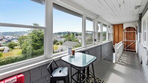 A room with large windows, a table, two chairs, and a view of a residential area.