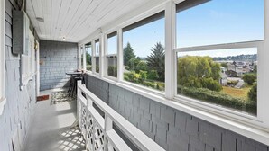 A covered porch with a view of a residential area, a brick wall, and a white railing.