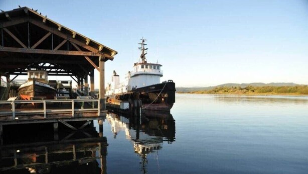 A docked ship at a calm harbor with a wooden pier and a clear sky.