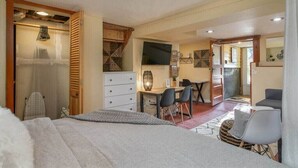 Une chambre à coucher avec un lit, un bureau et une chaise. Il y a un téléviseur accroché au mur et une fenêtre.
