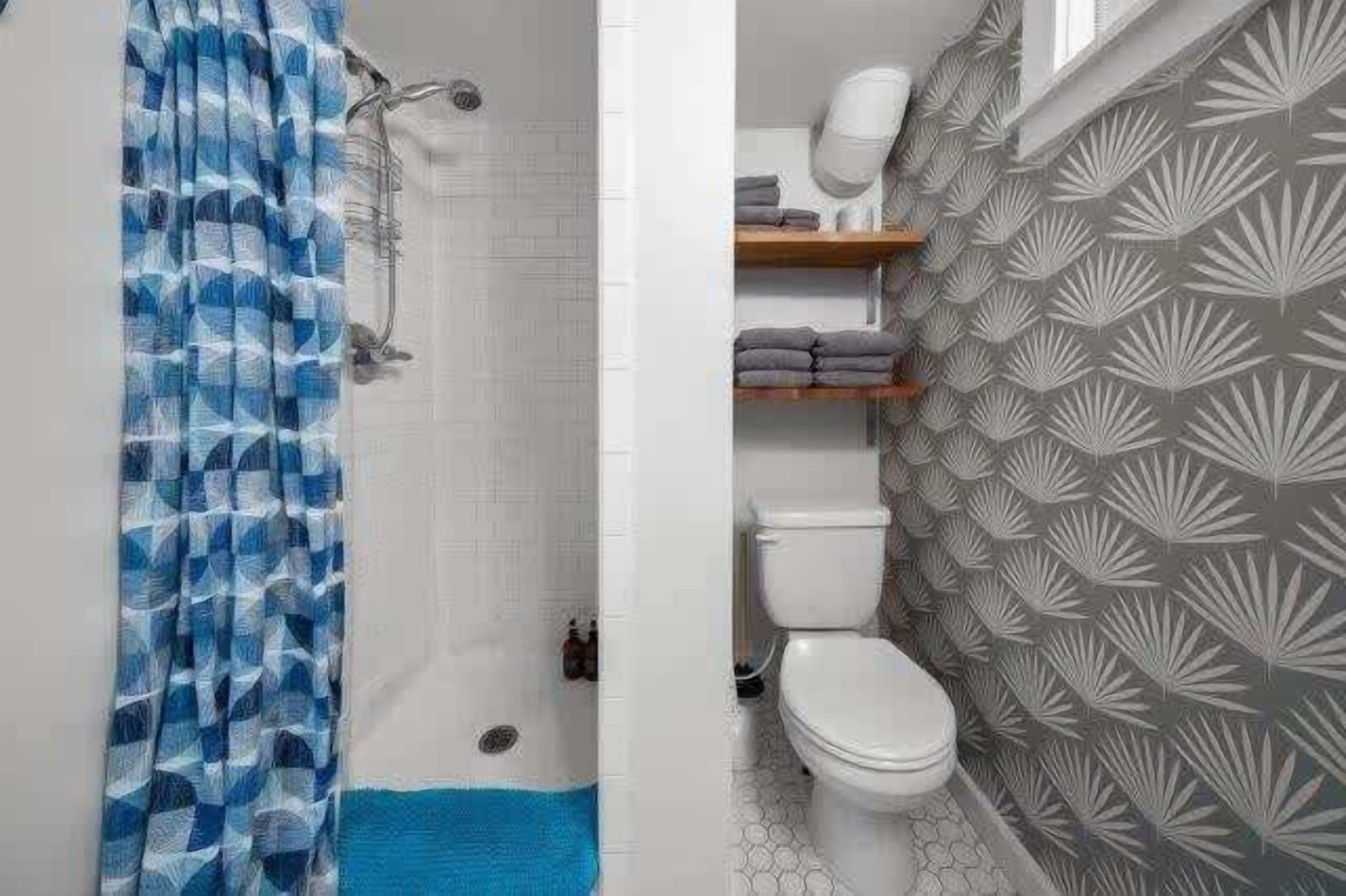 A bathroom with a shower curtain, toilet, and shelves with towels.