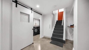 A hallway with a sliding door leading to a laundry area, a staircase with a red accent, and a clean, modern interior.