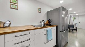 A modern kitchen with white cabinetry, a stainless steel refrigerator, and a wooden countertop.