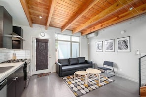 A modern kitchen with a stove, oven, and a black sofa in a living area with a coffee table and a patterned rug. - #StayinMyDistrict Buckman Open Loft-Style Townhome (Portland)