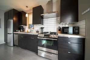 A modern kitchen with dark cabinetry, stainless steel appliances, and a tiled backsplash.