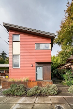 A modern two-story house with a red exterior, a front door, and a small porch area.