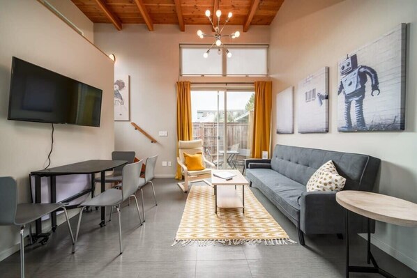 A modern living room with a flat-screen TV, a sofa, a coffee table, and a dining area with chairs.