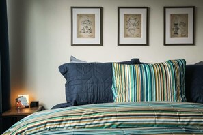 A bedroom with a bed, pillows, a bedside table, and framed wall art.