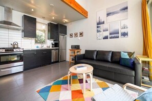 A modern kitchen with dark cabinets, a stove, and a microwave. There's a black sofa with cushions and a colorful rug.