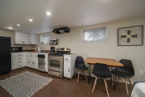 A compact kitchen with white cabinets, a stove, and a dining area with a table and chairs.