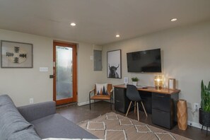 A living room with a sofa, a desk with a computer, a TV, and a door with frosted glass.
