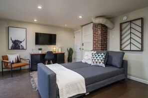A bedroom with a bed, a desk, a chair, a television, and a brick fireplace.