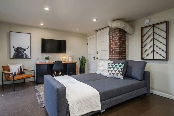 A bedroom with a bed, a desk, a chair, a television, and a brick fireplace.