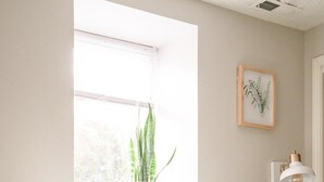 A bedroom with a bed, a window, a plant, and a wall-mounted lamp.