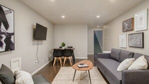 A modern living room with a gray sofa, a coffee table, and a TV mounted on the wall. There is a staircase in the background leading to another level.
