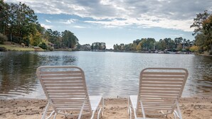 Deux fauteuils de relaxation en métal blanc, placés face à un lac, avec vue sur des arbres et des bâtiments au loin.