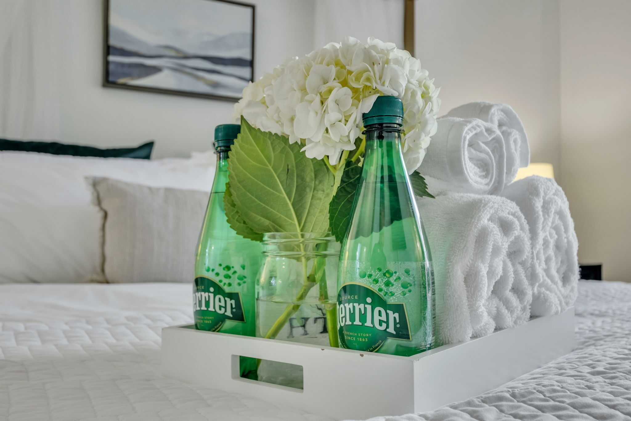 Un lit avec une literie blanche, une serviette blanche et trois bouteilles d’eau Perrier avec des étiquettes vertes.