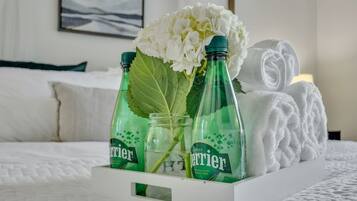 Un lit avec une literie blanche, une serviette blanche et trois bouteilles d’eau Perrier avec des étiquettes vertes.