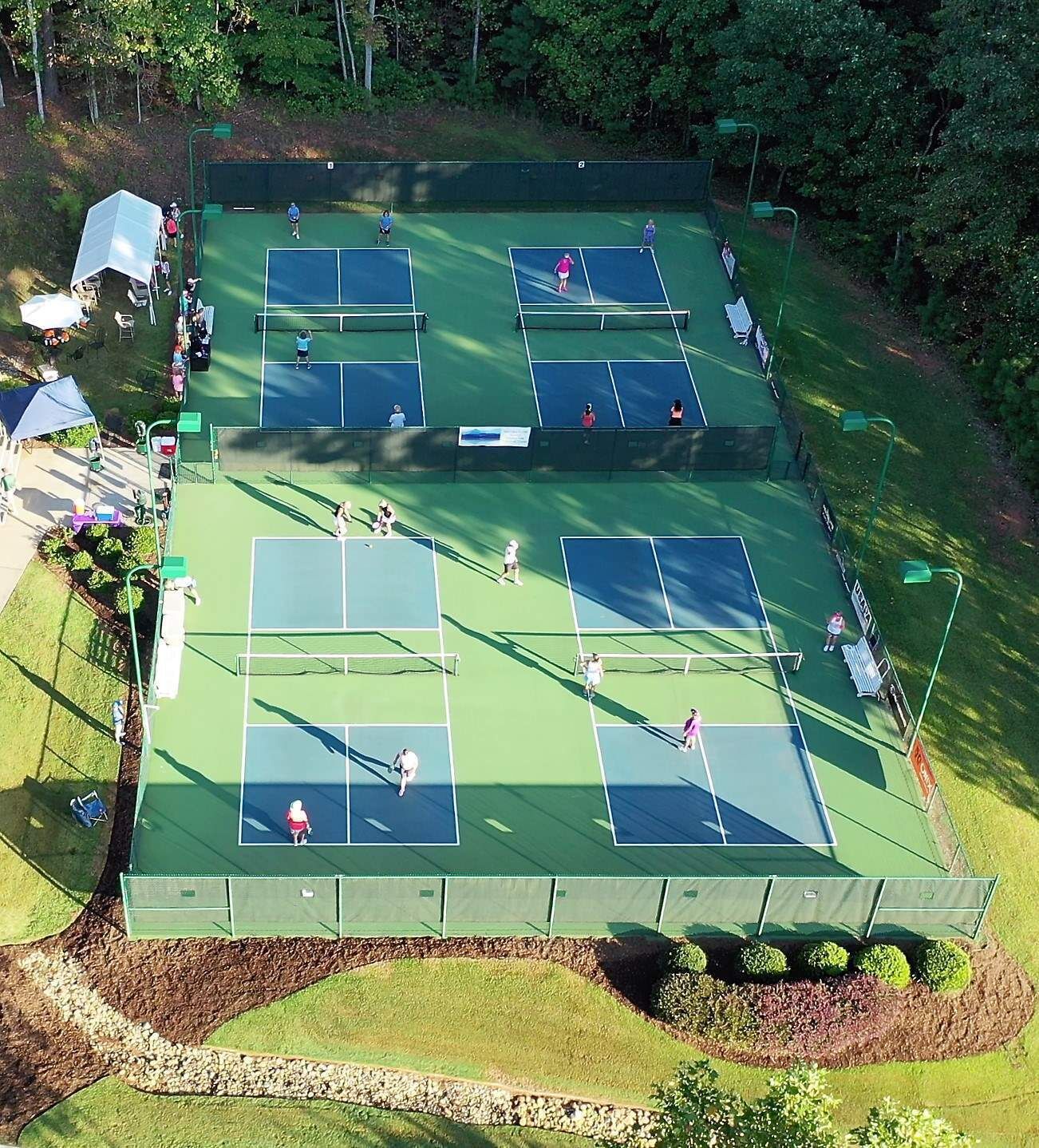 Un complexe de courts de tennis comprenant plusieurs terrains, des zones d’assise et un pavillon couvert.