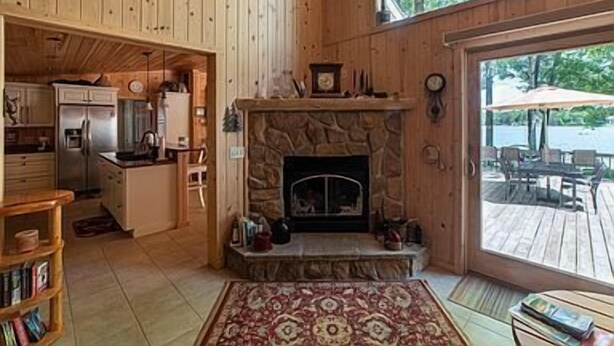 Interior de una cabaña de madera con cocina, chimenea y vistas a una terraza con mobiliario exterior.