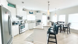 Una cocina moderna con armarios blancos, electrodomésticos de acero inoxidable y una isla central con taburetes de bar.