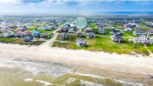 Vista aérea de una zona residencial costera con casas, una playa y cielo despejado.