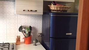 Uma cozinha com armários de madeira clara, uma geladeira azul, um fogão a gás e uma cesta de vime sobre a geladeira.