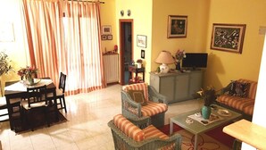Uma sala de estar com área de jantar, um sofá, uma televisão e uma luminária.