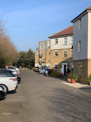A row of parked cars along a paved street in a residential area with multi-story buildings.