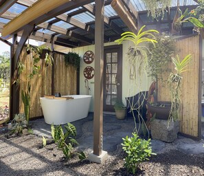 Une salle de bain privative dotée d’une baignoire sur pieds, entourée de différentes plantes en pot et d’un mur en bambou.