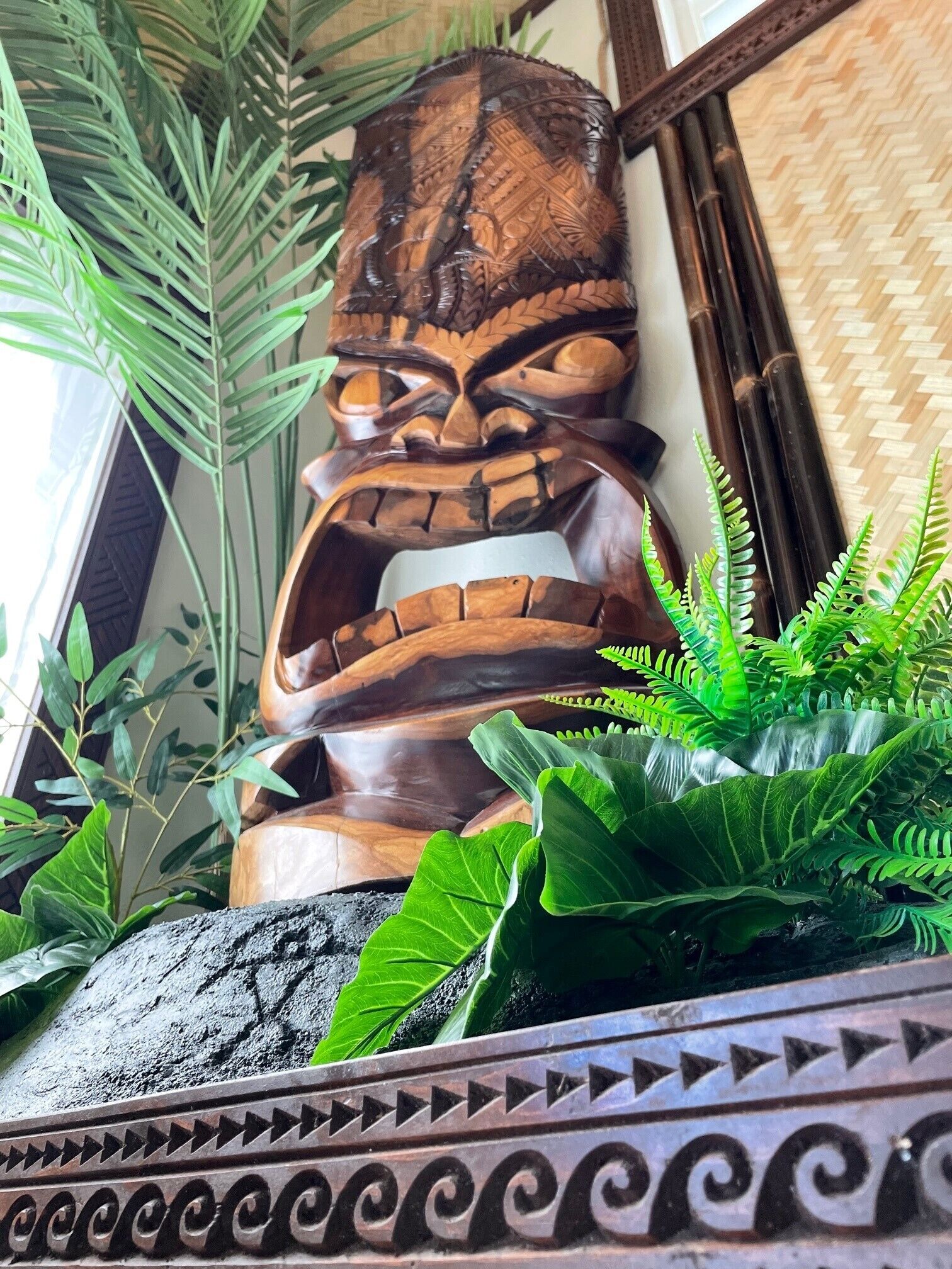 Een houten tiki-beeldje omgeven door weelderige groene planten.