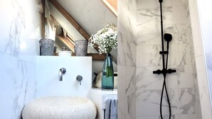 A bathroom with a stone sink, a shower with a handheld head, and a vase with flowers.