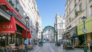A street with cafes and shops, a green archway, and a flower market.