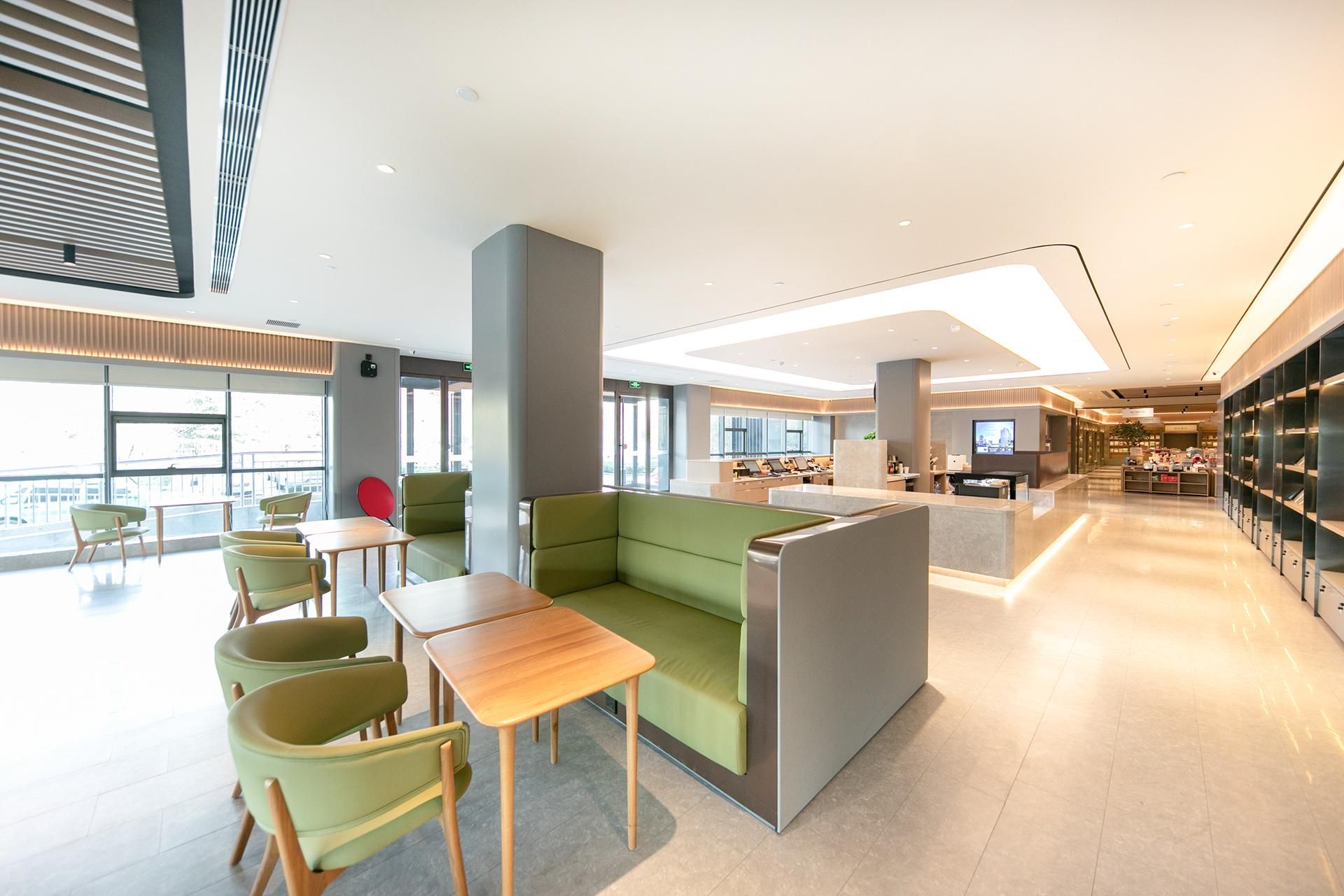 Um lobby moderno de hotel com áreas de estar, balcão de recepção e vista para a cidade.