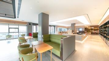 Um lobby moderno de hotel com áreas de estar, balcão de recepção e vista para a cidade.