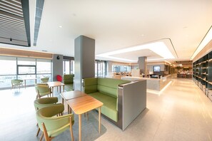 A modern hotel lobby with seating areas, a reception desk, and a view of the city. - Ji Hotel (Binzhou)