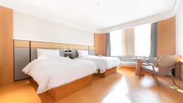 Quarto de hotel moderno com duas camas, área de estar e uma grande janela.