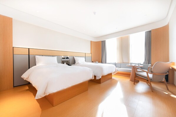 A modern hotel room with two beds, a seating area, and a large window.