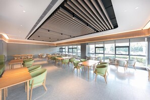A modern dining area with tables and chairs, large windows, and a sloped ceiling with lighting fixtures. - Ji Hotel (Binzhou)