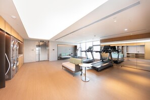 A modern hotel gym with exercise equipment, a seating area, and a large window providing natural light.