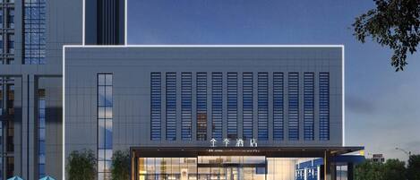 A modern hotel with a large glass facade, a prominent entrance, and a parking area in front.