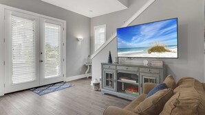 Una sala de estar con un televisor de pantalla plana grande en la pared, un sofá gris y un mueble de madera con un juego de Monopoly.