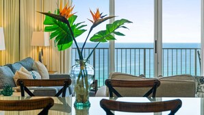 A room with a view of the ocean, a dining table with chairs, a sofa, and a vase with plants.