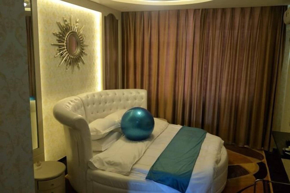 A hotel room with a tufted headboard, a large blue exercise ball, and a striped blanket.
