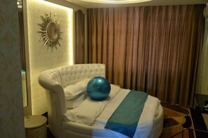 Une chambre d’hôtel avec une tête de lit capitonnée, un grand ballon bleu pour faire de l’exercice et une couverture à rayures.