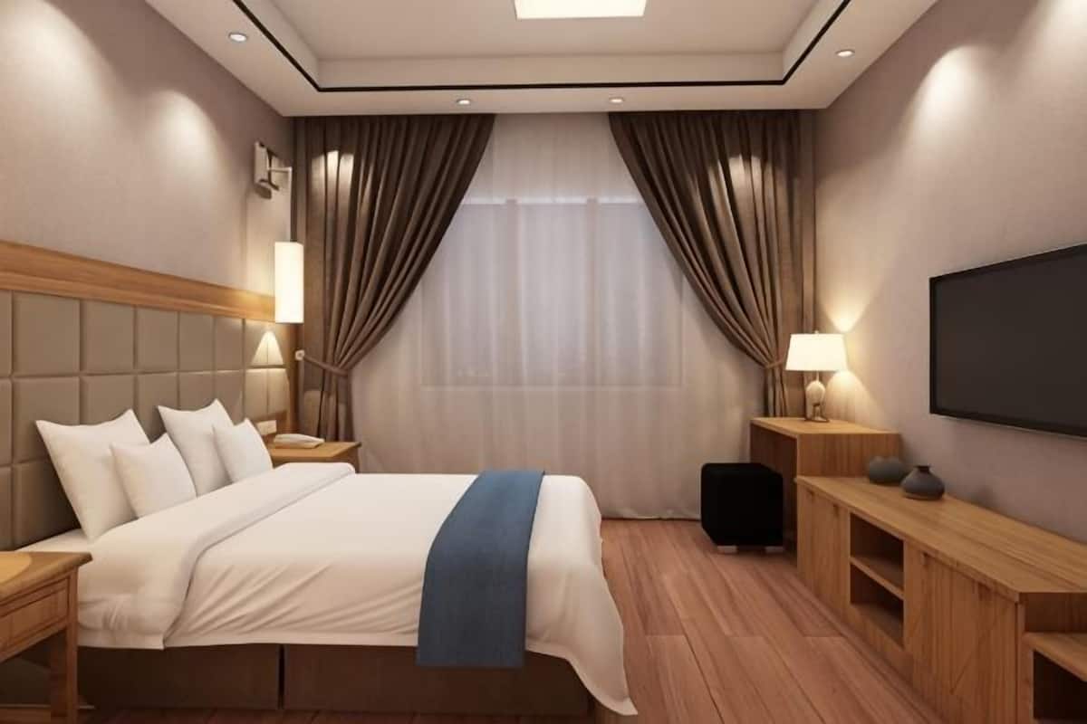 A hotel room with a bed, bedside tables, a TV, and a window with curtains.