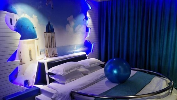 A hotel room with a bed, a blue exercise ball, a nightstand, and a wall mural. - Fenglinxuan Hotel (Ulaan Chab)