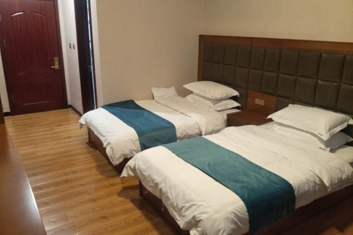 Camera d'albergo con due letti, pavimento in legno, una porta e una testiera imbottita.