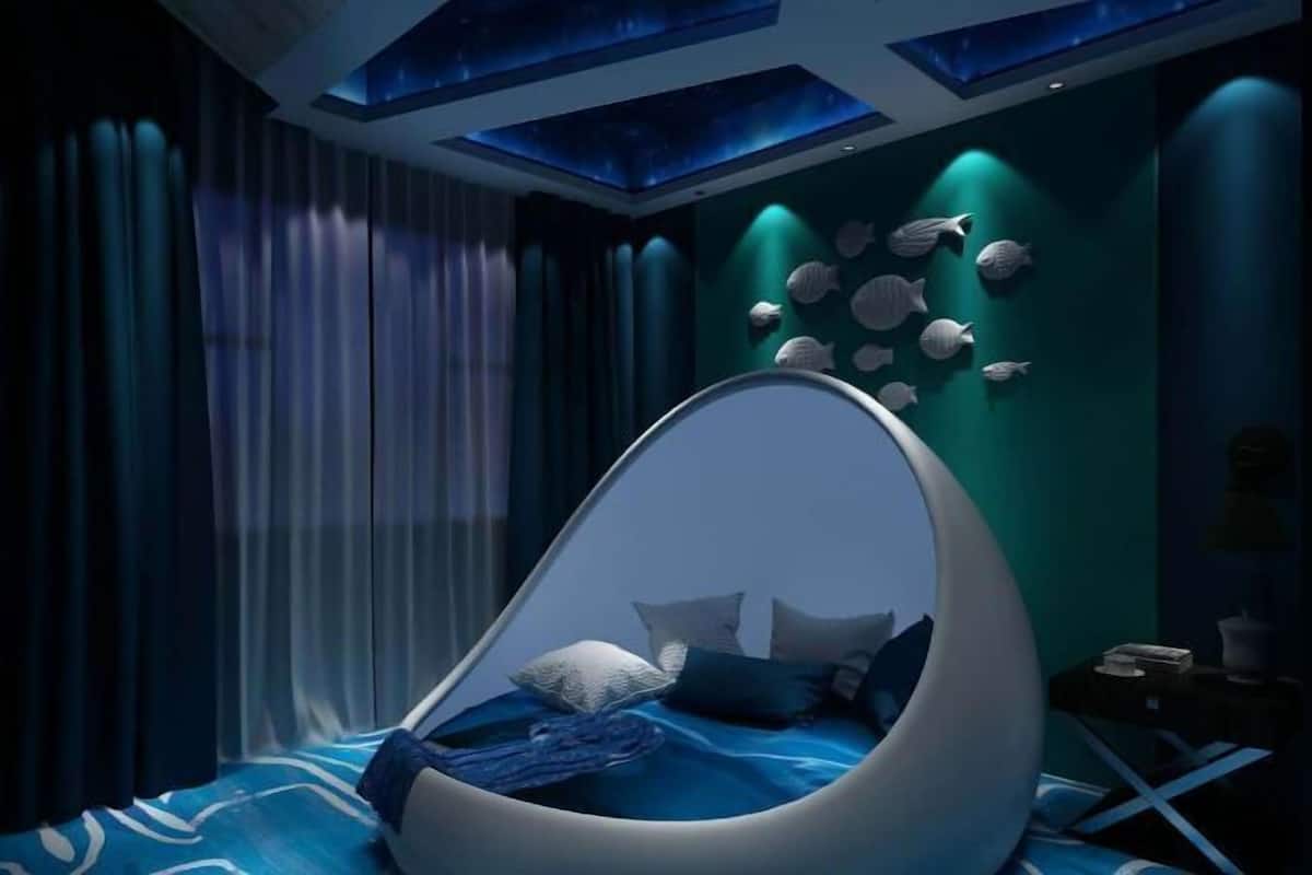 A modern room with a unique egg-shaped bed, a wall of fish decorations, and a ceiling with blue lighting.