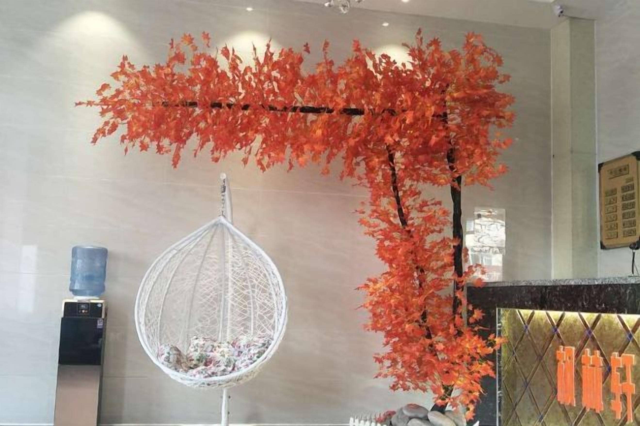 A room with a hanging chair, a water dispenser, and a decorative red tree branch.